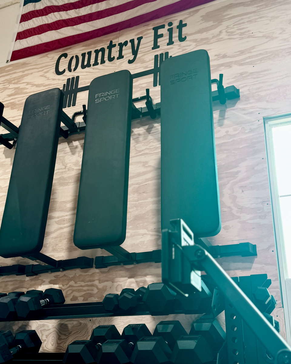Workout benches racked on the plywood wall below the hand-painted Country Fit sign.